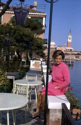 Phyliss Snider sitting on a white cement bench next to two white tables and chairs