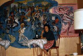 Phyliss Snider sitting at a cafe table with with two paintings behind her