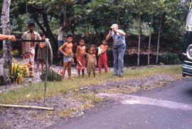 Children standing next to a man taking a picture of a snake held up on a stick