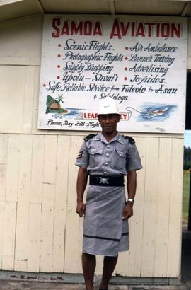 Man dressed in a military type uniform standing in front of a sign titled "Samoa Aviation"