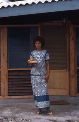 Woman standing at the entrance of a house holding a plate of fruit