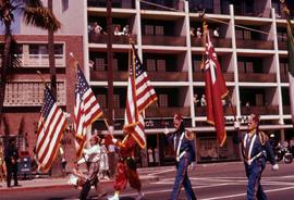 Four Shriners in uniform marching with flags