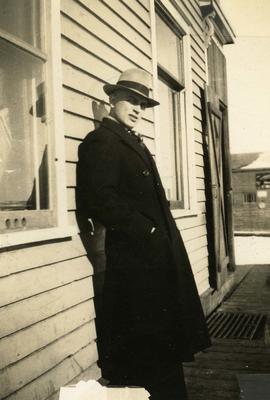 [Unidentified man leaning up against a house]