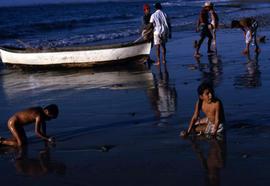 Two children playing on a beach with people and a boat in the background