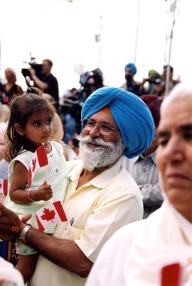 [A man in a blue turban holding a young girl with a Canadian flag]