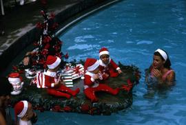 Young children in Santa costumes sitting by a pool next to a Christmas tree