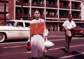 Man wearing a Shriner hat with his face painted white wearing a sign around his neck