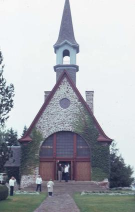 Church with two people standing on the steps and waving and three people standing on the grass