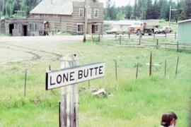 Sign for Lone Butte with a log house in the background