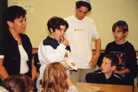 [Group of children watching one child eating challah and honey]