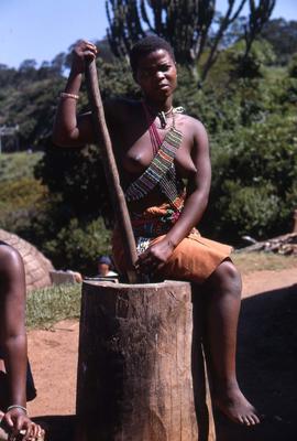 Unidentified South African woman sitting on a tree stump, in traditional ethnic attire