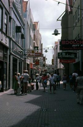 People walking along a walkway between two buildings with many signs