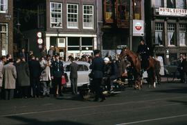 Crowd of people gathered outside on the street around a car