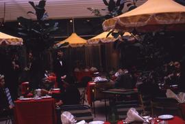 Patrons at a restaurant sitting at table with red tablecloths and yellow umbrellas