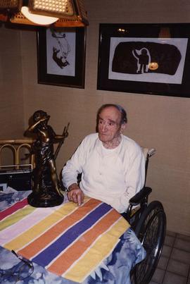 [Harry Nemetz sitting in his wheelchair next to a table with a bronze statue on it]