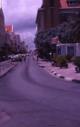 Street with buildings on either side and a kiosk on the right with a sign that reads: "Coca ...