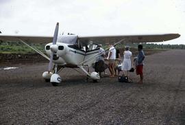 Group of people standing on a gravel runway either waiting to board or exit a small airplane