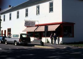 Cars on a street and a store with a red and white awning and a sign