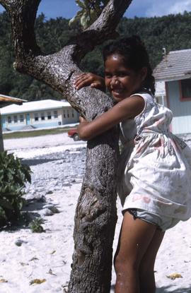 Girl hugging a tree on a white sandy beach]