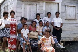 Group of women and girls in front of a wooden building