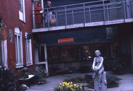 Statue of a female figure in the foreground and two women standing on a walkway in the background