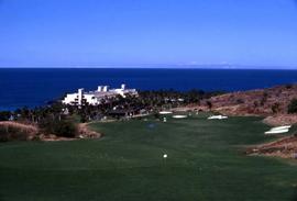 Golf course with a white building and the ocean in the background