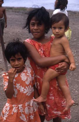 Two young girls in dresses, one holding a little child