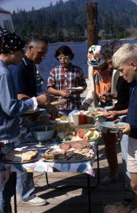 Group of people with plates in their hands standing around a table with food on it