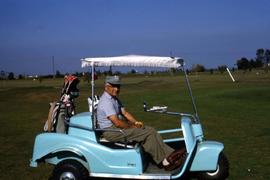 Dr. Irving Snider facing the camera while sitting in a light blue golf cart