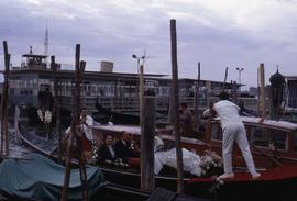 People sitting in a gondola with gondoliers standing on either end with wooden posts in the foreg...