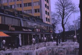 Tables and chairs outside of a building with several signs on it, one of which reads "Teen&q...