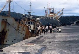 Workers standing on a dock next to ships from Korea and Norway