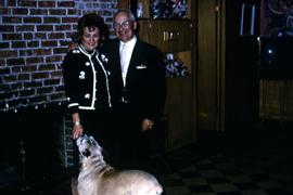 Dr Irving and Phyliss Snider and their dog posing in front of a fireplace